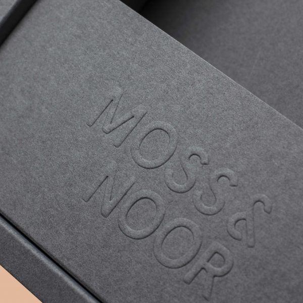 Närbild på efterbehandlingen emboss på en grå Moss & Noor förpackning